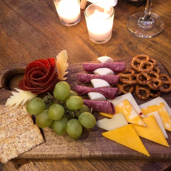 Charcuterie board with salami, cheeses, grapes, crackers, and pretzels, lit by candles.