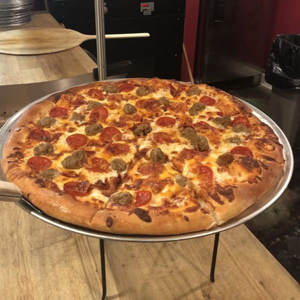 A freshly baked Bourbon Street Pizza with pepperoni and sausage on a metal stand.