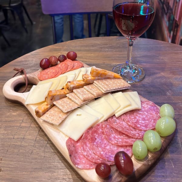 A charcuterie board with cheeses, salami, crackers, and grapes, next to a glass of red wine.