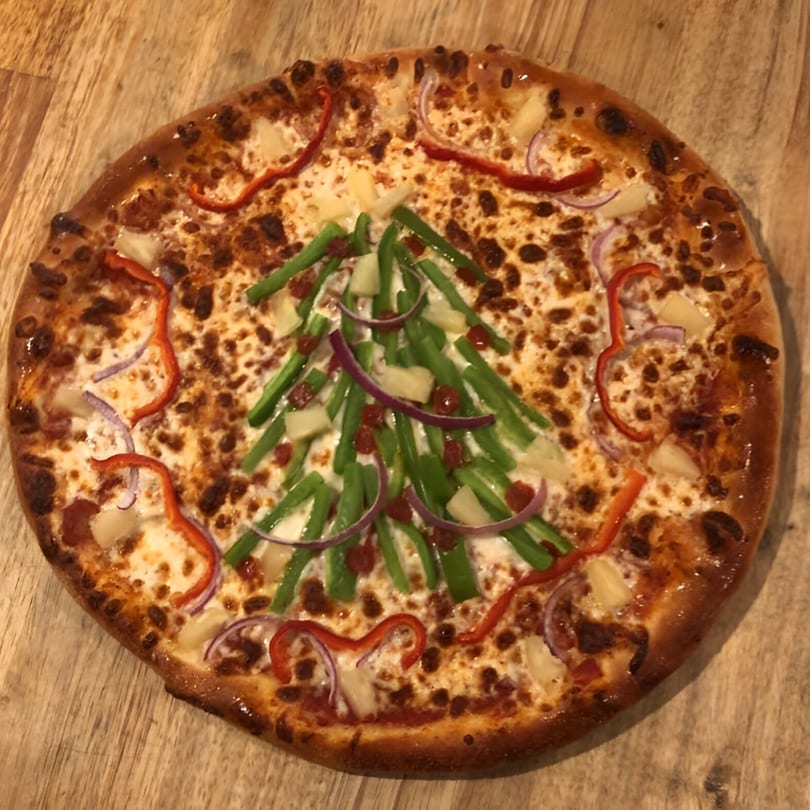 Bourbon Street Pizza with a Christmas tree design made from green peppers, red peppers, and onions.