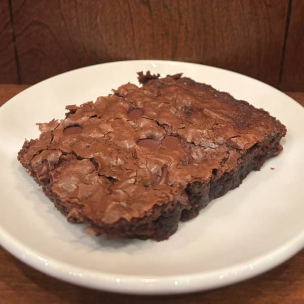 A rich, fudgy brownie with chocolate chips and a crinkled top, served on a white plate.