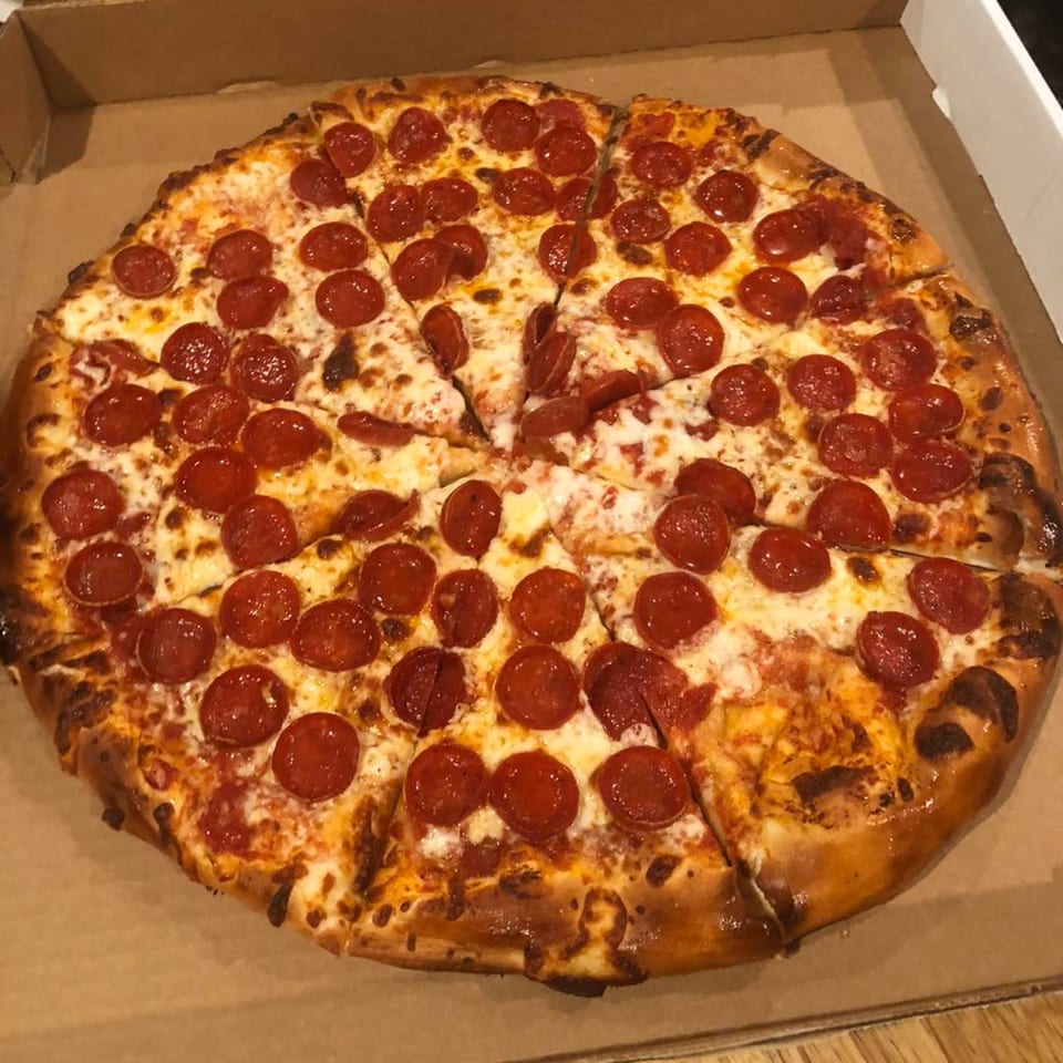 A large, freshly baked pepperoni pizza from Bourbon Street Pizza & Wine Bar, sliced and in a cardboard box.