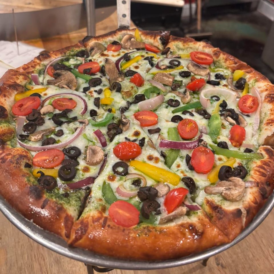 A freshly baked Bourbon Street Pizza with vibrant vegetables, including tomatoes, olives, mushrooms, and peppers.