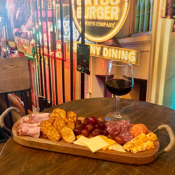 A charcuterie board with meats, cheeses, crackers, and grapes, next to a glass of red wine.