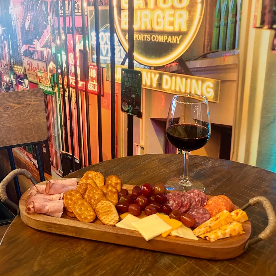 A charcuterie board with meats, cheeses, crackers, and grapes, next to a glass of red wine.